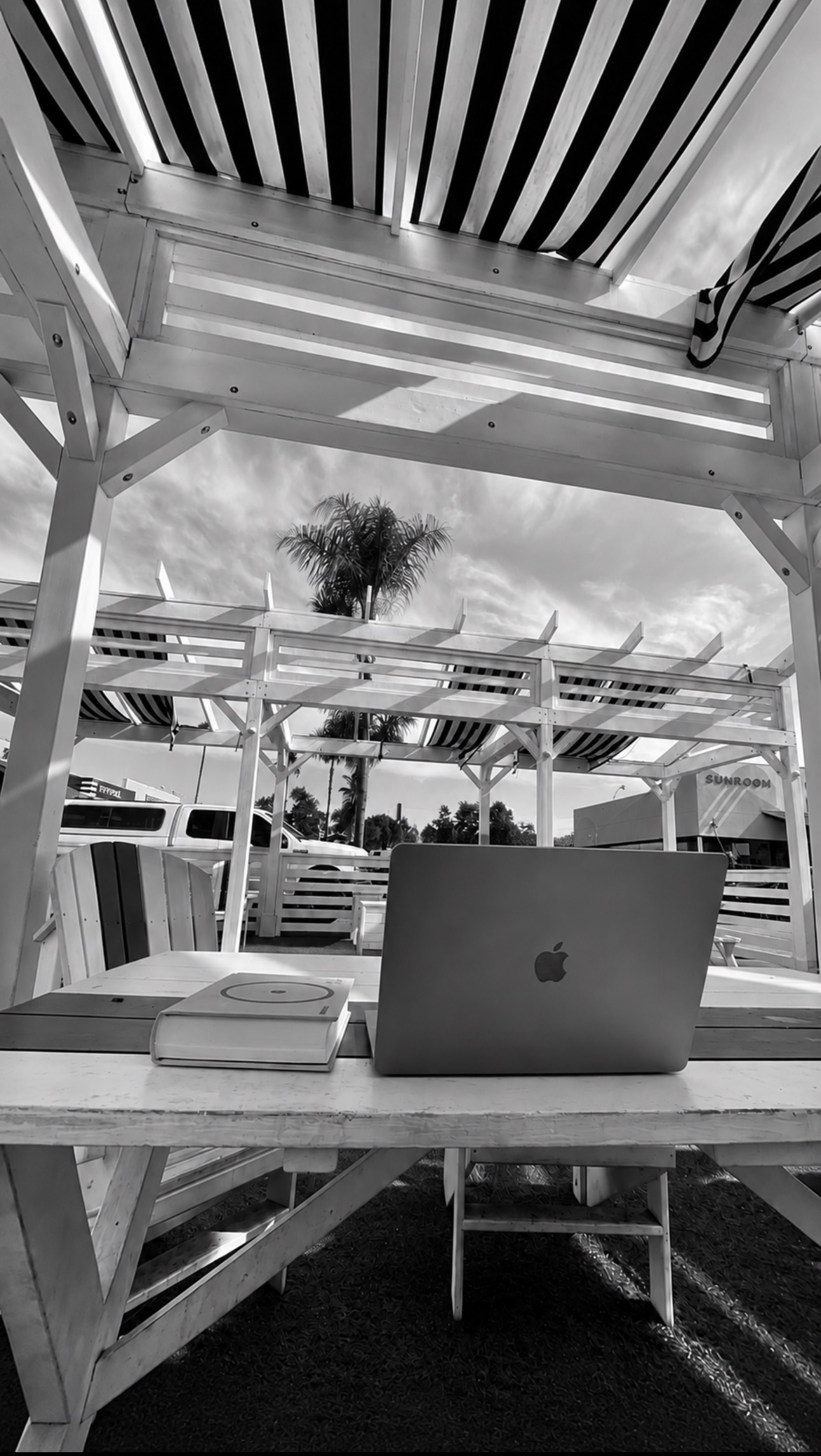 Laptop on an outdoor table beneath geometric beams and palm trees